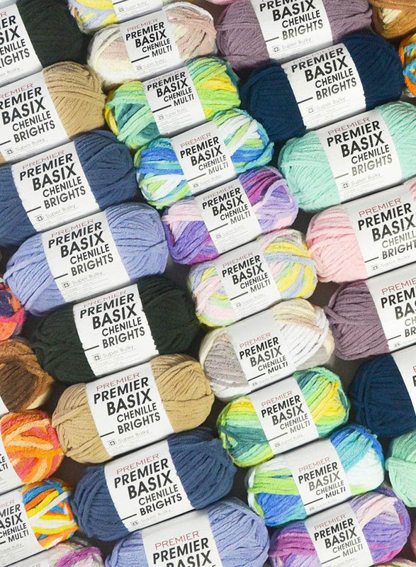 A colorful assortment of Premier Basix Chenille yarn skeins arranged in a diagonal pattern. The skeins come in a variety of solid and multicolored shades, including bright, pastel, and neutral tones. Each skein is wrapped with a white label - Premier Basix Chenille